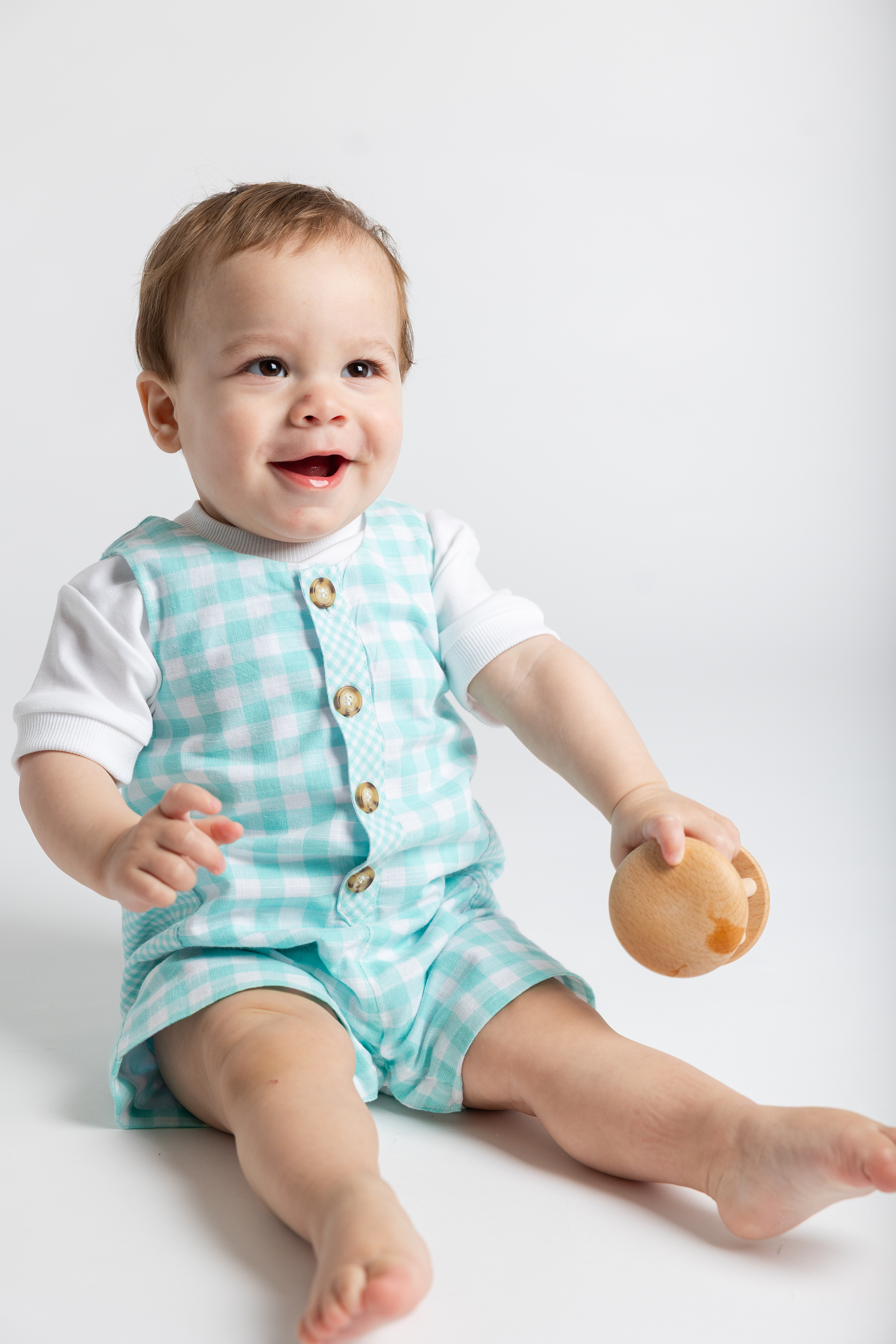 Young boy sitting on the floor in a teal plaid shortall and white t-shirt
