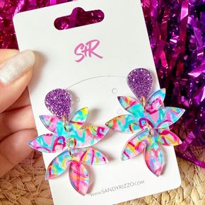 Featuring a playful mix of purple, blue, pink, and yellow graffiti-inspired design topped with shimmering purple glitter, these dangles bring bold, artistic flair to any look.